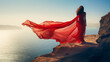 © Anna - Woman in red dress standing on a cliff by the sea. Sense of freedom. The wind blows in the long veil. Creativity portrait photography. Travel and fashion concept. AI generative.