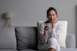 Asian woman feels toothache while drinking cold water sitting on sofa at home. Female having dental health problems