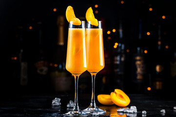 Wall Mural - Apricot Bellini cocktail drink with sparkling wine and apricot puree, syrup and ice, dark bar counter background with bottles