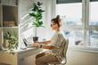 © olezzo - Young adult Caucasian woman in glasses working on a laptop in a modern apartment office near the window