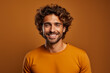 Handsome man with curly hair happily poses against brown background 