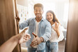 © Prostock-studio - Hello. Happy indian spouses meeting somebody standing near opened door, man stretching hand for handshake