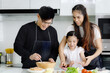 © Stella - Happy family cooking at kitchen, father mother and cute daughter girl having fun during making meal at home. Parents and kid child enjoy cooking food, spending time together. Family love and bonding.