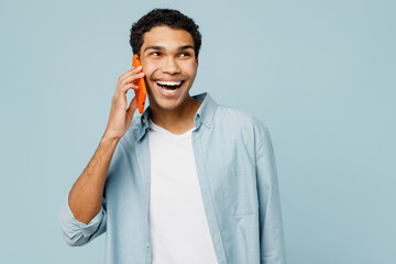 Wall Mural - Young man of African American ethnicity wear shirt casual clothes talk speak on mobile cell phone conducting pleasant conversation isolated on plain pastel light blue cyan background studio portrait.