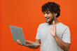 Side view young happy Indian man wearing t-shirt casual clothes hold use work on laptop pc computer waving hand talk speak isolated on orange red color background studio portrait. Lifestyle concept.