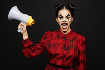 Wall Mural - Young woman with Halloween makeup face art mask wearing clown costume red dress hold in hand megaphone screaming isolated on plain solid black background studio portrait. Scary holiday party concept.