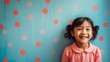 Happy cute Asian toddler girl wearing Polkadot colorful dress smiling and standing in front of blue and red painted wall, girl portrait with copy space.