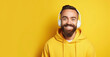 Cute young guy with a beard wearing yellow big headphones, yellow hoodie smiles and looks at the camera on yellow background. Young hipster man listening to music, modern student listening to lecture 