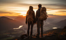 Couple Of Man And Woman Hikers On Top Of A Mountain At Sunset Or Sunrise, Together Enjoying Their Climbing Success And The Breathtaking View, Looking Towards The Horizon
