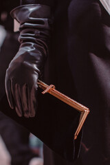 Wall Mural - A female hand in a black leather glove holding a classic velvet clutch with a gold frame. Vertical fashion shot