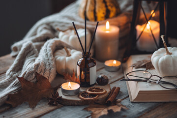 Home comfort, coziness, aromatherapy. Cozy fall interior with knitted wool warm sweater, burning candles and autumn aroma perfume diffuser. Pumpkin pie scent, maple sirup, cinnamon, anise, dry citrus