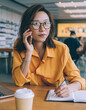 © BullRun - Satisfied female writing notes while talking on phone