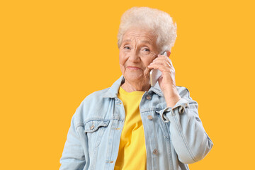 Wall Mural - Senior woman talking by mobile phone on yellow background