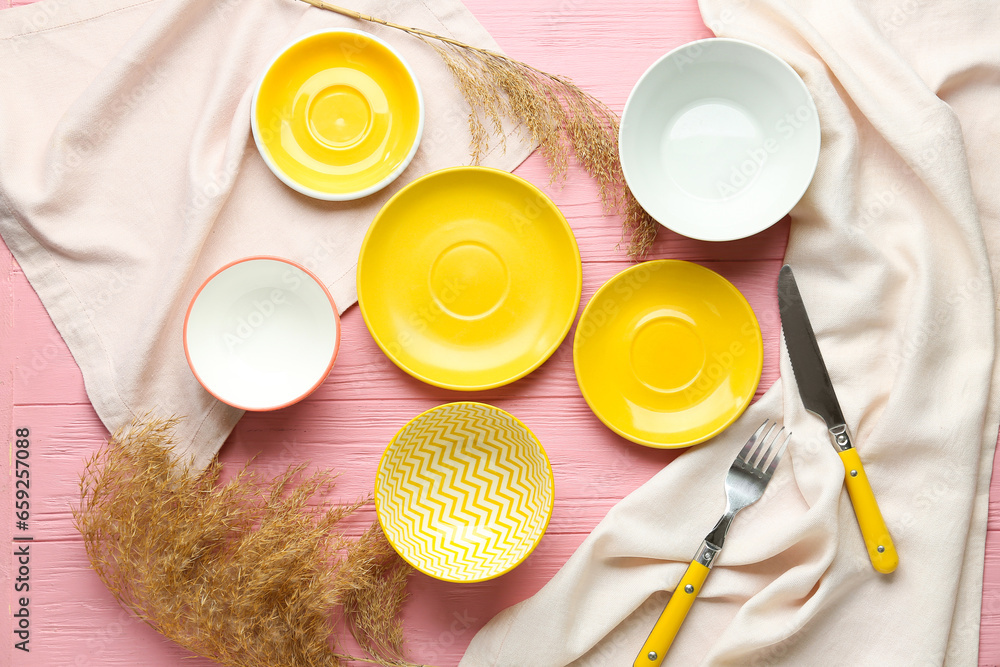Clean plates, cutlery and dried grass on pink wooden table