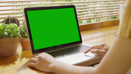 Over the shoulder shot of woman, using finger with keyboard for typing touch. computer laptop with blank green screen chroma key in cafe.