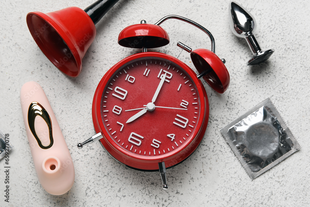 Alarm clock with different toys and condom on grunge white background. Time for sex