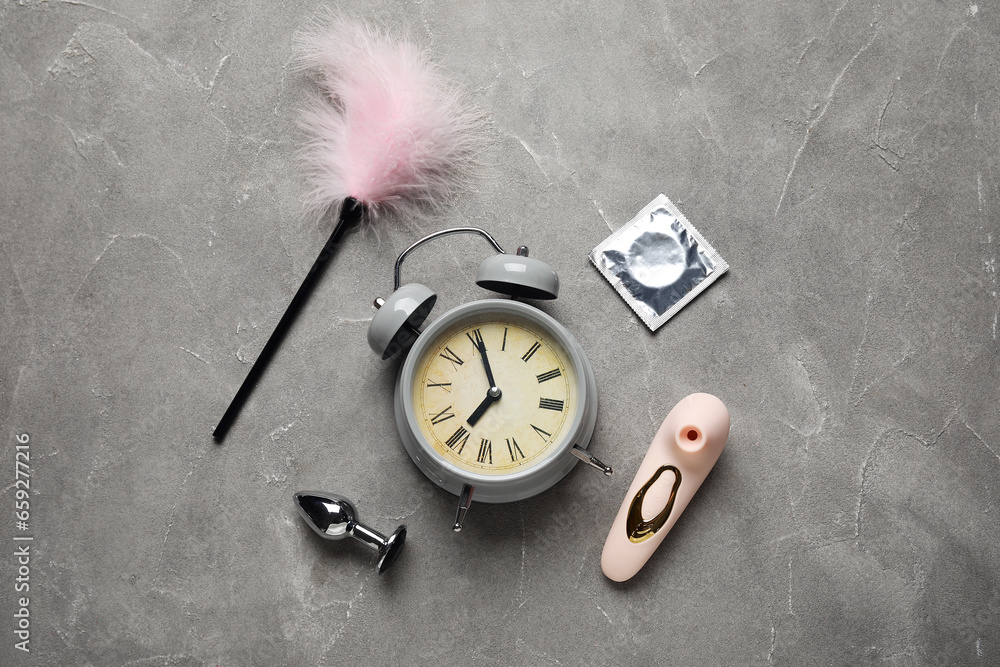 Alarm clock with different toys and condom on grunge grey background. Time for sex