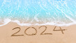 2024 new year goals planning concept. Numbers 2024 on brown sand and blue ocean waves. Top view.Investment in 2024. Copy space for your design or text. Wallpaper background