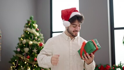 Sticker - Young hispanic man holding christmas gift dancing at home