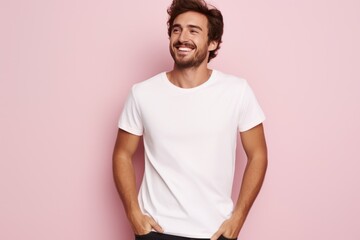 Wall Mural - Portrait of a happy 30 - year - old man wearing a white t shirts with hands in pocket next to a light pink pastel background. Mock up t shirt concept.