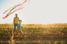 Playful Father And Son Flying Kite In Field On Sunny Day