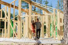 Couple Standing At Wooden Construction Frame On Sunny Day