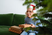 Happy Girl Holding Christmas Presents Sitting On Sofa At Home
