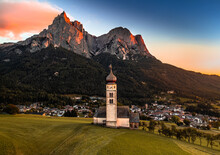 Seis Am Schlern, Italy - Aerial View Of St. Valentin Church And Famous Mount Sciliar Mountain At Background At Sunset With Golden And Blue Sky And Warm Sunlight At South Tyrol On A Summer Afternoon