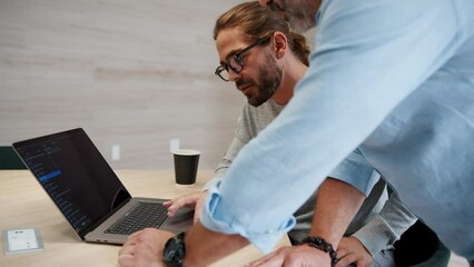 Two software engineers brainstorming tech solutions using laptop, they discuss a code they're working on. Business men collaborating on a software design project in a tech startup.