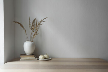 Wall Mural - Elegant moody Scandinavian interior. Vase with dry grass bouquet, old books and little white pumpkins. Empty wall background. Modern living room, home office. Minimal autumn decor in cozy apartment.