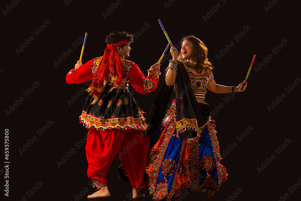 A happy young couple performing Dandiya Raas on a black background ...