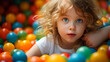 Happy little girl having fun in ball pit in kids indoor play center. Child playing with colorful balls in playground ball pool.