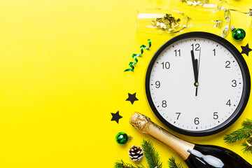 New year celebration concept with a bottle of champagne and two glasses toasting. Christmas gift box, alarm clock and fir tree branch on colored table. Top view Copy space