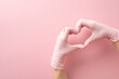 © ActionGP - Embracing my medical journey. First person top view of female medic's hands, clad in surgical gloves, craft a heart gesture on soft pink. A canvas for your message