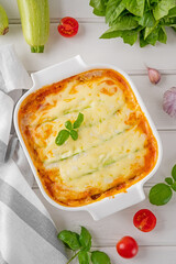 Wall Mural - Delicious zucchini lasagna with sauce bolognese in a baking dish on a white wooden bachground. Healthy food. Top view. Selective focus.