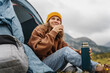 © olezzo - A young cheerful woman traveling with a tent drinks hot tea from a thermos. Hiking and trekking concept