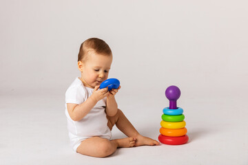 Little boy playing logic educational games with plastic pyramid isolated on white background. A happy child plays with an educational toy. The baby is one year old