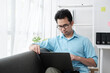 © Parichat - Young attractive man sitting on sofa at home working on laptop online, using internet, smiling, happy mood, freelancer, free leisure time, relaxed, modern job lifestyle