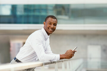 Young African American Businessman Standing Outdoors, Holding Smartphone And Smiling At Camera