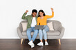 © Prostock-studio - Excited indian couple shaking fists over laptop sitting on sofa