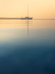 Wall Mural - sea view to sailboat on calm water in golden hour