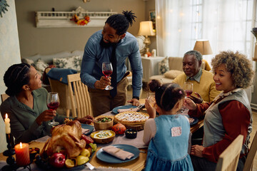 Happy black man raising a toast during family meal on Thanksgiving.