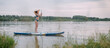 A young woman with an open swimsuit swims on a SUP board on a picturesque lake. Evening tour. A beautiful, slender girl is engaged in sap surfing on the calm water of a picturesque pond.