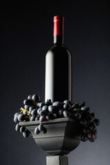 Poster - Blue grapes and a bottle of red wine on a black background.