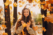 Smiling Positive Young Woman Throws Up The Yellow Autumn Leaves In The Forest At Sunset