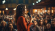 Young female speaker standing on stage in front of audience with microphone. View from the back. Training, speech, report at the conference. 