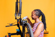 African American female cyclist carefully examines and repairs bike components with specialized tools and lubricant for smooth performance. Black woman diligently greasing and servicing bicycle chain.