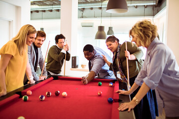 Wall Mural - Young and diverse group of business friends playing pool in the modern office