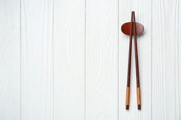 Wall Mural - Pair of chopsticks with rest on white wooden table, top view. Space for text