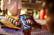 © Marko Geber - Young African American woman taking pictures of sushi on a smartphone in a sushi restaurant or bar